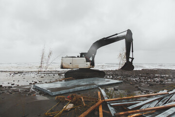 An excavator drives along an embankment destroyed after a storm and hurricane among garbage and...