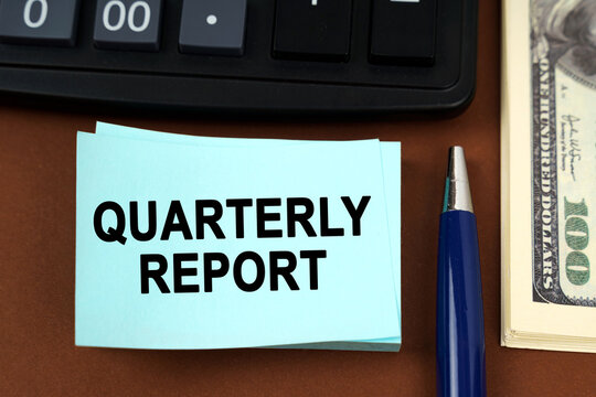 On a brown surface lies a calculator, dollars, pens and stickers with the inscription - quarterly report