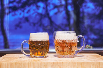 Two pints of lager beer pilsner type form Czech Republic in the traditional czech style mugs in front of window during the cold winter evening. Special kind of beer is traditional drink for Christmas.