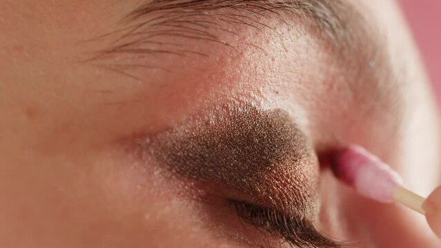 Closeup shot, style artist applies black mascara on the eyelashes of the female eye. Woman making make up using pink mascara. Professional makeup. Making mua. Smoky eyes