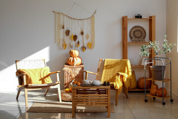 Interior of stylish living room with wooden furniture, armchairs and pumpkins
