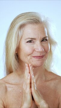 Vertical video portrait of mature senior woman looking at camera. Happy beautiful caucasian mature woman posing over white background