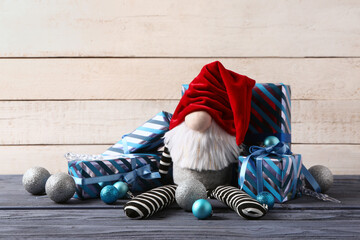 Christmas gnome with gift boxes and balls on blue wooden table against white background