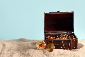 Old chest with treasures and compass on sand against blue background
