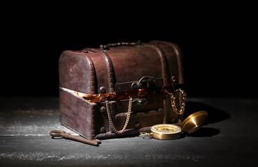 Old chest with treasures, key and compass on wooden table against black background