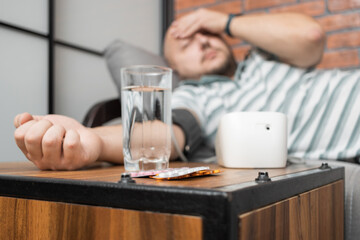 Defocused background with man who has hypertension and headache, lying on sofa at home, measures...