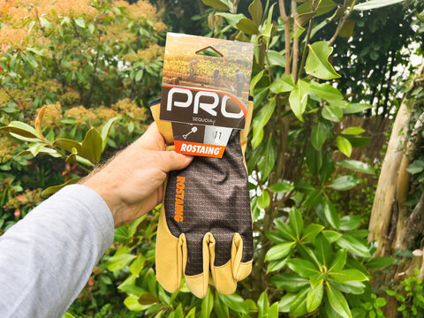 Paris, France - Apr 21, 2023: A male hand holding a new pair of working gloves from the Rostaing brand while in a garden setting, ready for some outdoor tasks