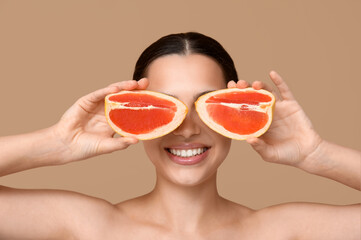 Pretty young woman with fresh grapefruit on beige background