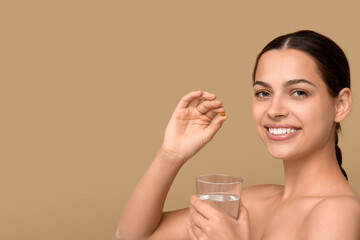 Pretty young woman taking vitamin A capsule on beige background