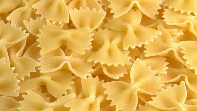 Authentic italian dry pasta farfalle rotating closeup background top view sunny. Raw dried organic golden macaroni, traditional Italy food