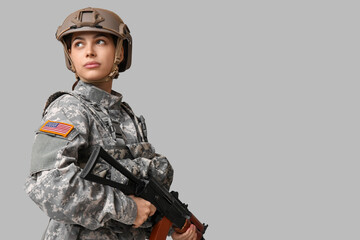 Confident young female soldier with assault rifle on grey background