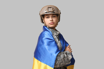 Young female soldier in uniform with flag of Ukraine on grey background