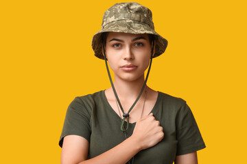 Confident young female soldier in uniform saluting on yellow background