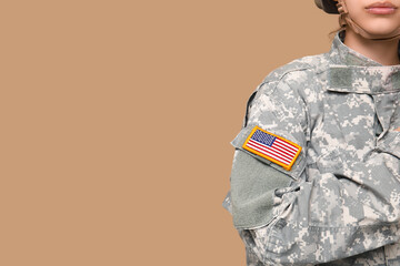 Confident young female soldier in uniform with American flag patch on sleeve saluting against beige background, closeup