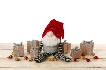 Christmas gnome with gift boxes and balls on beige wooden table against white background