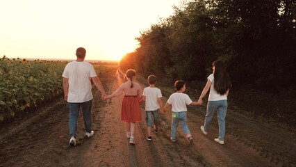Loving family with children walks joining hands along ground road in evening