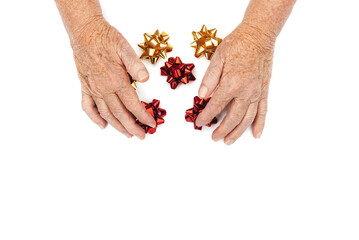 Old wrinkled female hands holding set of neon foil bows in red and gold colors on white background. Happy holidays. Copy space. View from above