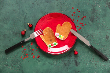 Plate with pancake in shape of mittens on green table. Christmas celebration