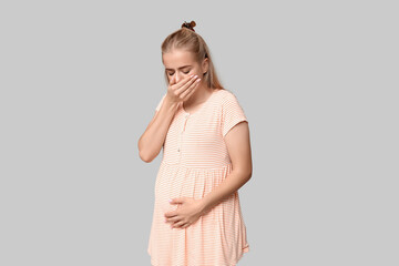Beautiful young pregnant woman suffering from toxicosis on grey background