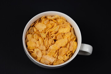 cornflakes in a white bowl on a black background, top view of the flakes