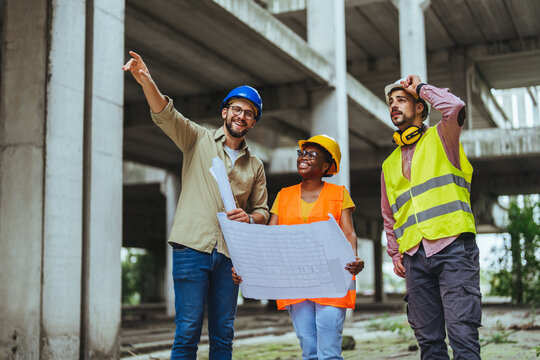 Comparing with the blueprints, a team of experts is evaluating the realization on the construction site. For their own safety, all members have yellow vests and hard hats.