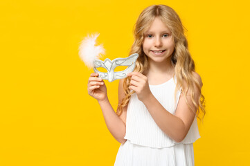 Funny little girl with carnival mask on yellow background