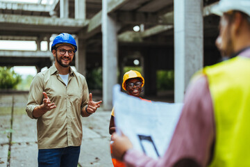 Group of civil engineers looking at blueprints at a construction site and wearing helmets. Mature...