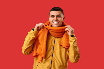 Young man in stylish jacket and scarf on red background