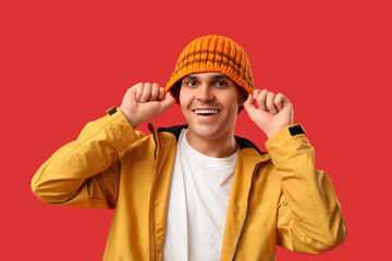 Young man in stylish jacket and hat on red background
