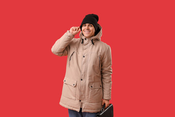Young man in stylish puffer jacket and hat with bag on red background
