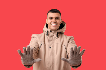 Young man in stylish puffer jacket and gloves on red background