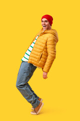 Fototapeta premium Young man in stylish puffer jacket and hat on yellow background