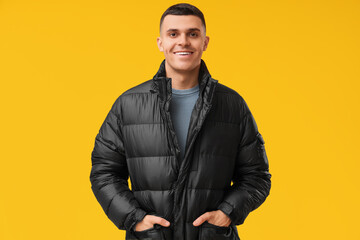 Young man in black stylish puffer jacket on yellow background - obrazy, fototapety, plakaty