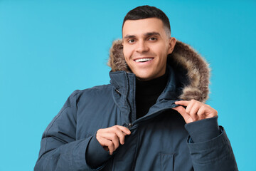 Young man in stylish puffer jacket on blue background