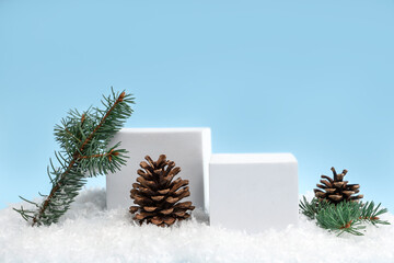 Decorative podiums with Christmas tree branches and pine cones on snow against blue background