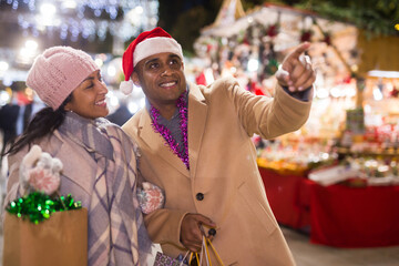 Happy married couple point finger at selected christmas tree decorations at street market