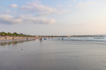 BALI, INDONESIA - OCTOBER 10, 2023: Tourists and locals on famous Kuta beach in Kuta, Bali. This is the perfect place for learning surfing.