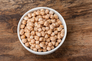 Top view image of raw chickpeas in a white ceramic bowl on vintage wooden table with copyspace
