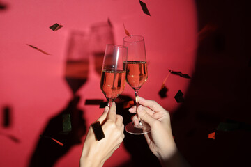 Female hands with glasses of champagne and confetti on red background