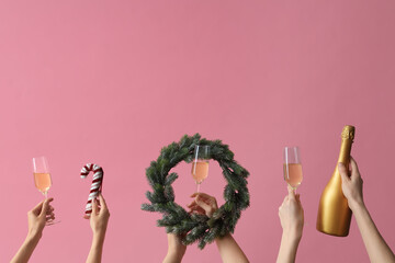 Female hands with glasses of champagne and wreath on pink background