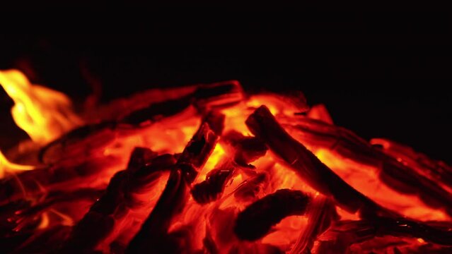 A pile of smoldering embers close up. Little tongues of flame and sparks appear on the coals.