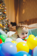 Fototapeta na wymiar A cute little boy is playing in a pool of plastic balls. Children's dry pool at home.