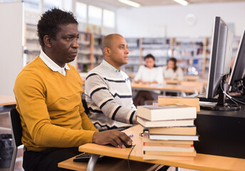 Focused adult African American sitting at table in pc room in public library. Self-study concept