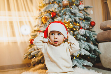 Cute little boy in santa hat with christmas tree. Children's New Year. Christmas tree. Christmas atmosphere at home.
