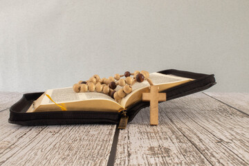 Open bible with rosary beads on wooden table - obrazy, fototapety, plakaty