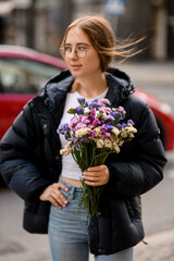 Fototapeta premium Wind develops the hair of a girl with a bouquet of multi-colored flowers on an autumn street