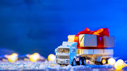 Toy truck carrying Christmas gifts, blue background, snow and garlands, copy space