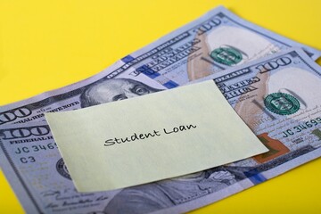 Close up debt reminder slip labeled ‘Student Loan’ posted to two one hundred dollar bills