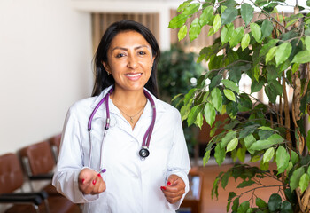 Portrait of young adult female doctor standing in office and friendly smiling, meeting patients