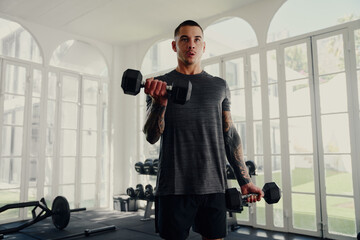 Young tattooed multiracial man in sportswear weight training at gym